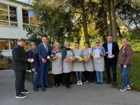 Die Gäste der Urkundenverleihung posieren für den Fotografen mit regionalen Produkten wie Honig und Gemüse bei Sonnenschein vor dem Schullandheim Reichmannshausen. 